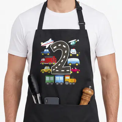 Transportation 2nd apron - Number two road shape surrounded by cartoon police car, taxi, train, plane, and helicopter — shown on a black cotton canvas apron against a white background