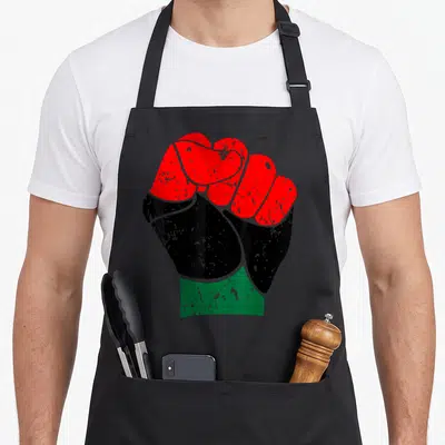 Fist pride apron - Clenched fist graphic with red, black, and green horizontal bands and distressed texture — shown on a black cotton canvas apron against a white background