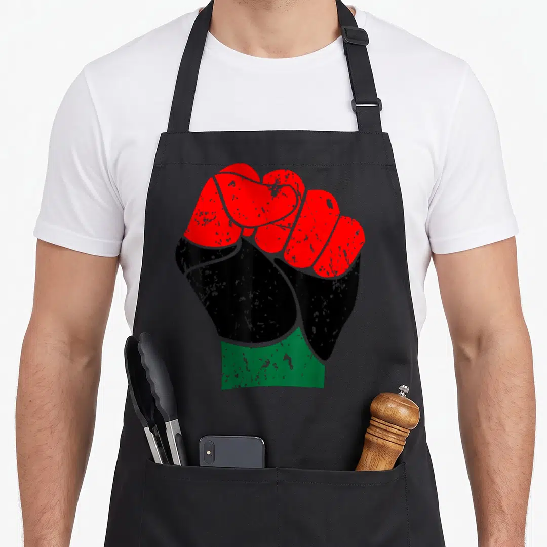 Fist pride apron - Clenched fist graphic with red, black, and green horizontal bands and distressed texture — shown on a black cotton canvas apron against a white background