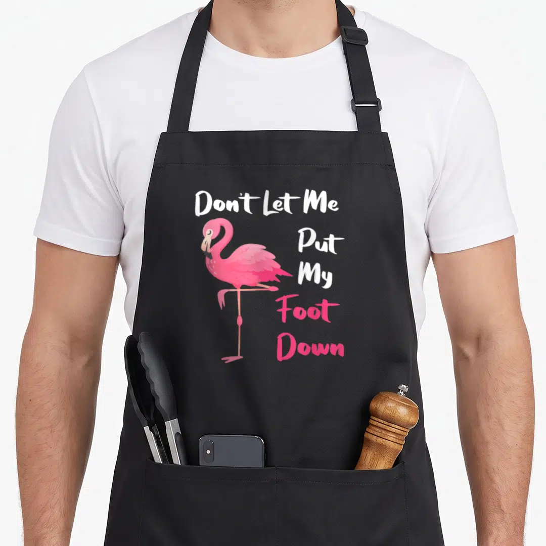 Foot pink flamingo apron for kids - Cartoon pink flamingo stands next to stacked white and pink text reading Don't Let — shown on a black cotton canvas apron against a white background