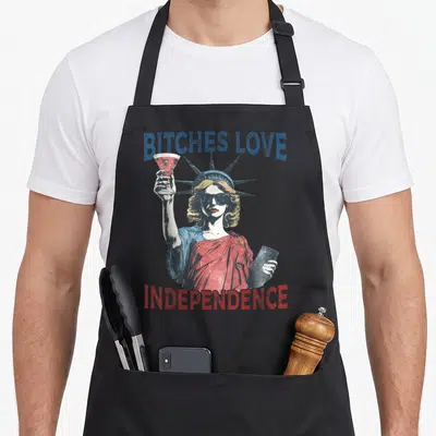 Independence patriotic 4th of july apron - Statue of Liberty holding cocktail and tablet with Bitches Love Independence — shown on a black cotton canvas apron against a white background