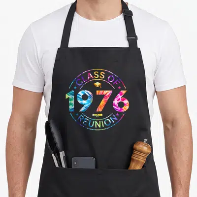 Classmate tie-dye apron - Tie-dye circle with Class of 1976 Reunion text, graduation cap, stars, and diploma scroll — shown on a black cotton canvas apron against a white background