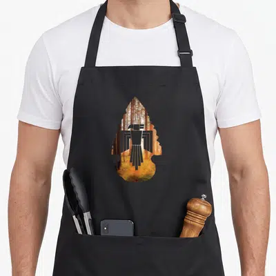 Native eagles grill apron - White eagle silhouette inside arrowhead shape filled with sunlit forest photo in orange — shown on a black cotton canvas apron against a white background