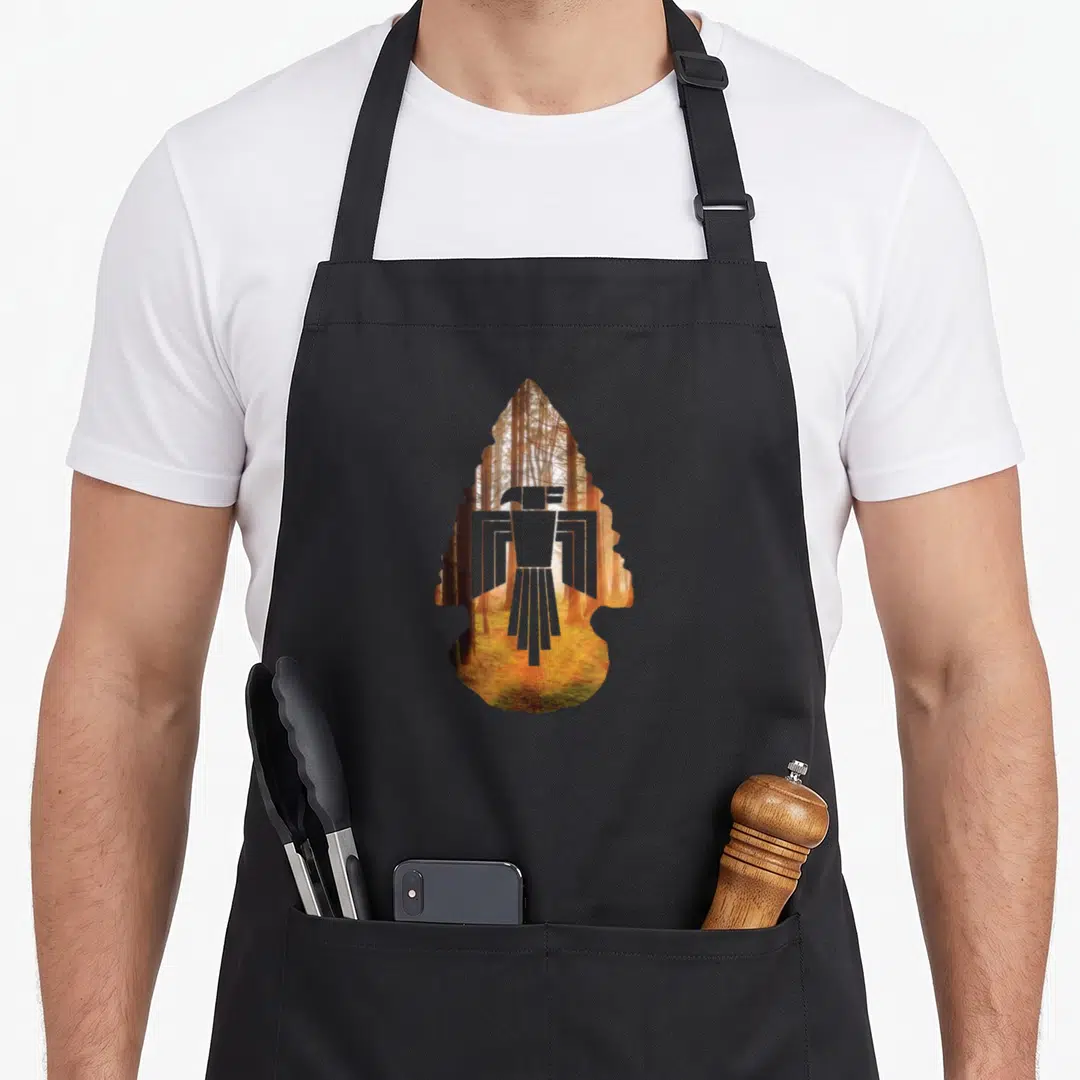 Native eagles grill apron - White eagle silhouette inside arrowhead shape filled with sunlit forest photo in orange — shown on a black cotton canvas apron against a white background