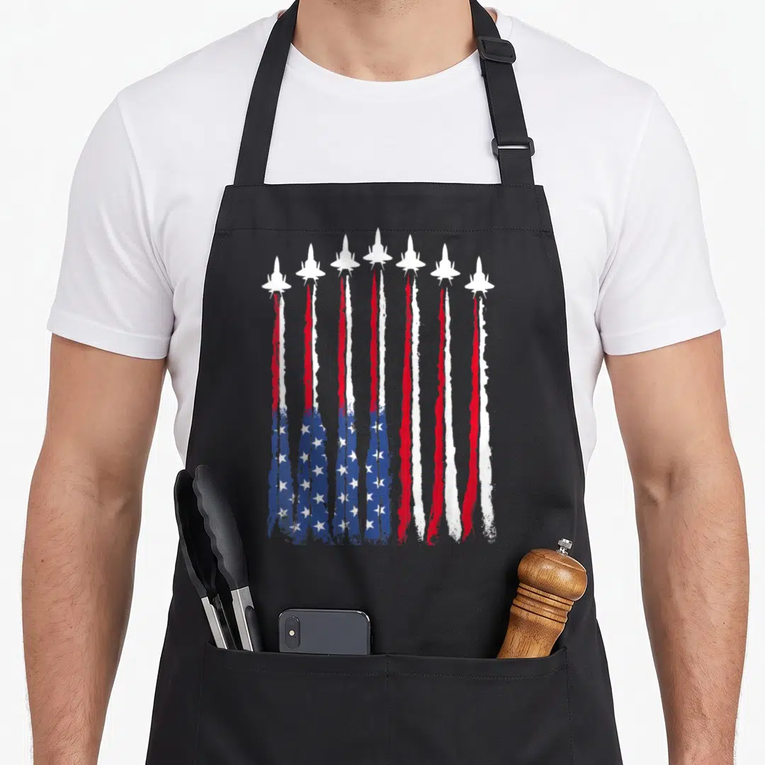 Patriotic 4th of july apron for women - Seven white jets flying upward leaving red white and blue smoke trails that — shown on a black cotton canvas apron against a white background