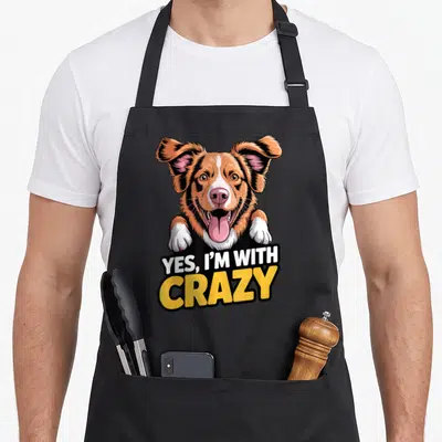 Dog cotton duck aprons - Cartoon dog peeking over Yes I'm With Crazy text — shown on a black cotton canvas apron against a white background