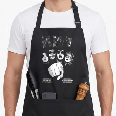 Funny kiss kissimmee apron - Distressed white KISS star logo, four band faces, pointing hand, and concert date text — shown on a black cotton canvas apron against a white background