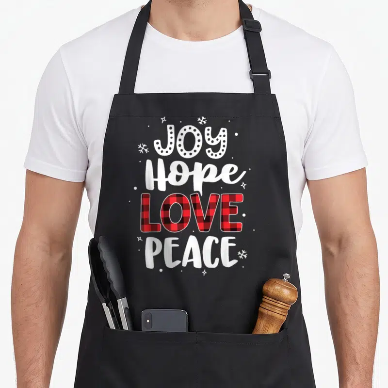 Joy buffalo plaid christmas apron - Stacked JOY Hope LOVE PEACE text with red plaid fill and white snowflakes — shown on a black cotton canvas apron against a white background