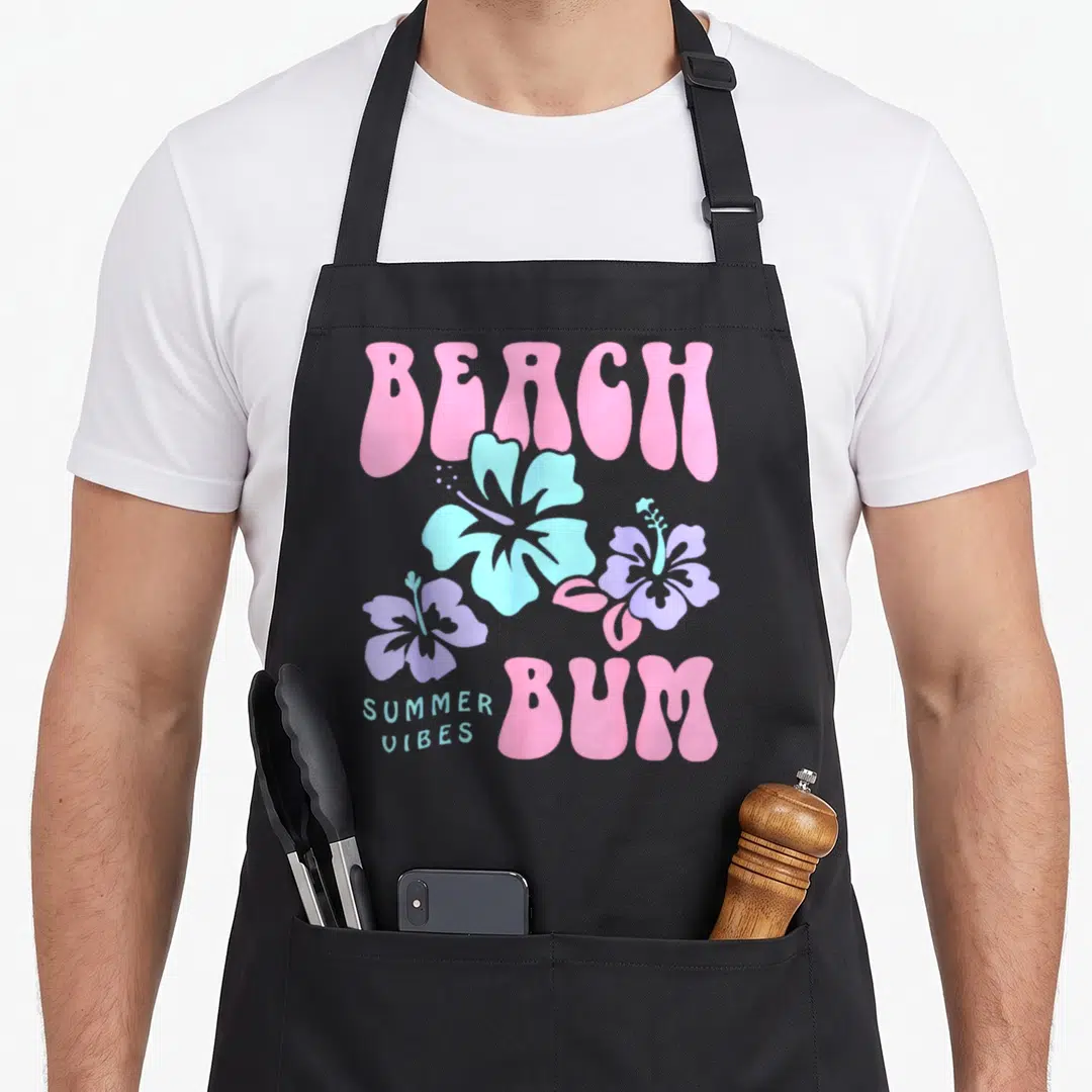 Coconut trendy apron - Retro pink and blue text reading Beach Bum surrounded by three pastel hibiscus flowers — shown on a black cotton canvas apron against a white background