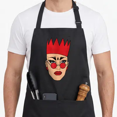 Velour queen apron - Cartoon head with red crown, red round glasses, tan skin, and black outlines — shown on a black cotton canvas apron against a white background