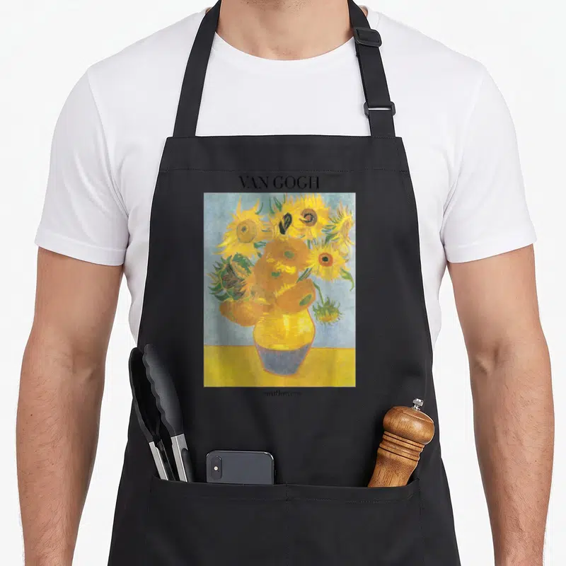 Sunflower vincent van gogh apron - VAN GOGH text above yellow sunflower painting with blue background and lower label — shown on a black cotton canvas apron against a white background