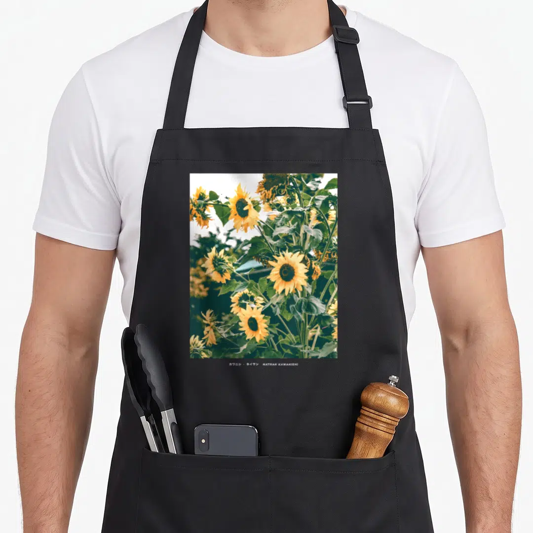 Floral streetwear apron - Sunflower photo with Nathan Kawanishi text on black apron — shown on a black cotton canvas apron against a white background