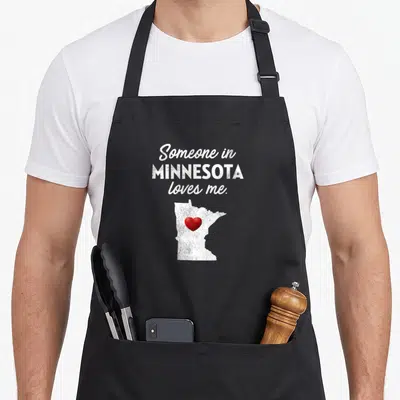 Someone minnesota apron - Stacked white text above white Minnesota silhouette containing a red heart on black fabric — shown on a black cotton canvas apron against a white background
