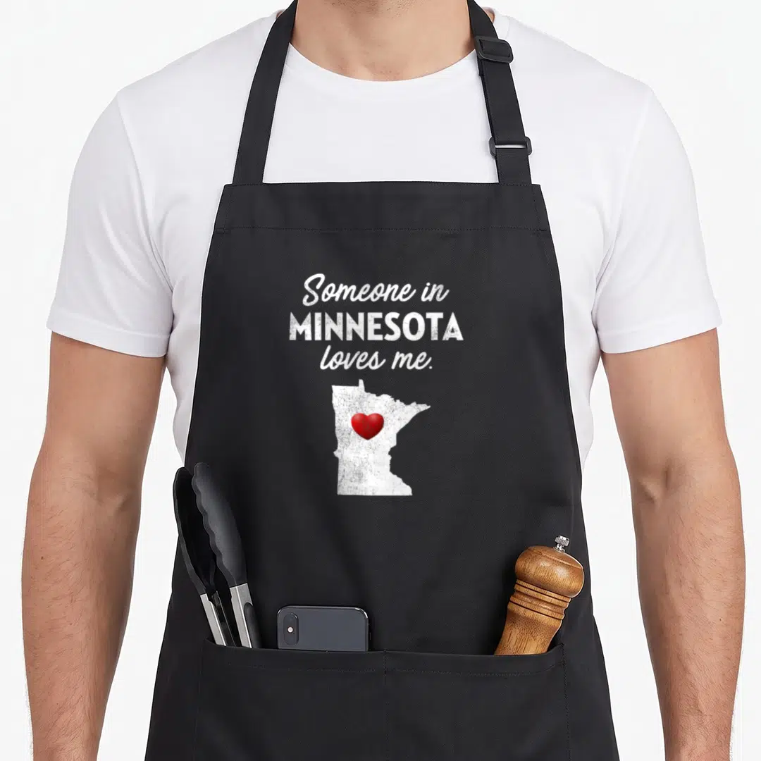 Someone minnesota apron - Stacked white text above white Minnesota silhouette containing a red heart on black fabric — shown on a black cotton canvas apron against a white background