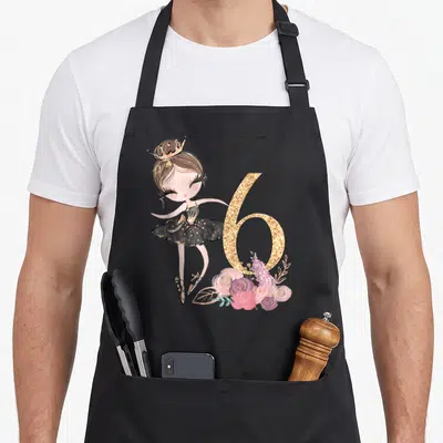 6th ballerina apron - Cartoon ballerina girl in black tutu next to glitter number 6 and pink purple flowers — shown on a black cotton canvas apron against a white background