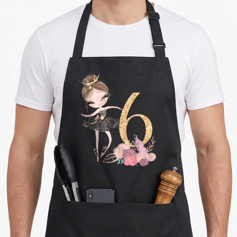 6th ballerina apron - Cartoon ballerina girl in black tutu next to glitter number 6 and pink purple flowers — shown on a black cotton canvas apron against a white background