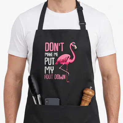 Foot animal pink flamingo apron - Pink flamingo standing on one leg beside stacked text reading Don't Make Me Put My — shown on a black cotton canvas apron against a white background