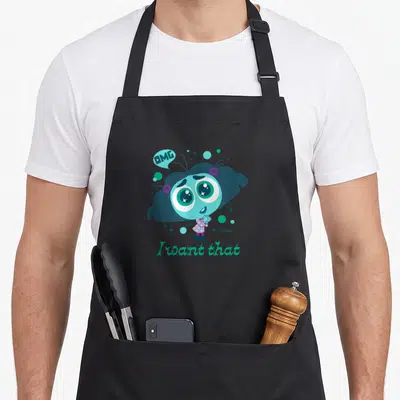 Envy character aprons - Cartoon character with I want that text and teal purple green stars — shown on a black cotton canvas apron against a white background
