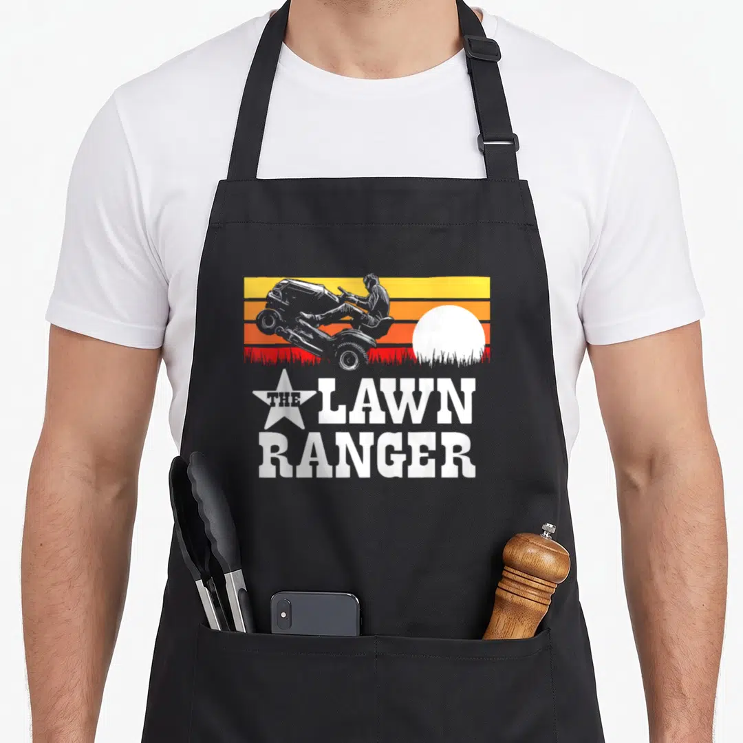 Mower rangers apron - Retro sunset graphic of person on riding mower doing wheelie with THE LAWN RANGER text in white — shown on a black cotton canvas apron against a white background