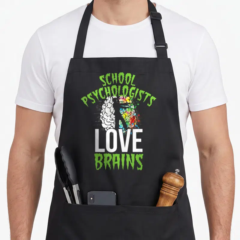 Brain halloween apron - Cartoon brain with silhouette and lime green text reading SCHOOL PSYCHOLOGISTS LOVE BRAINS — shown on a black cotton canvas apron against a white background