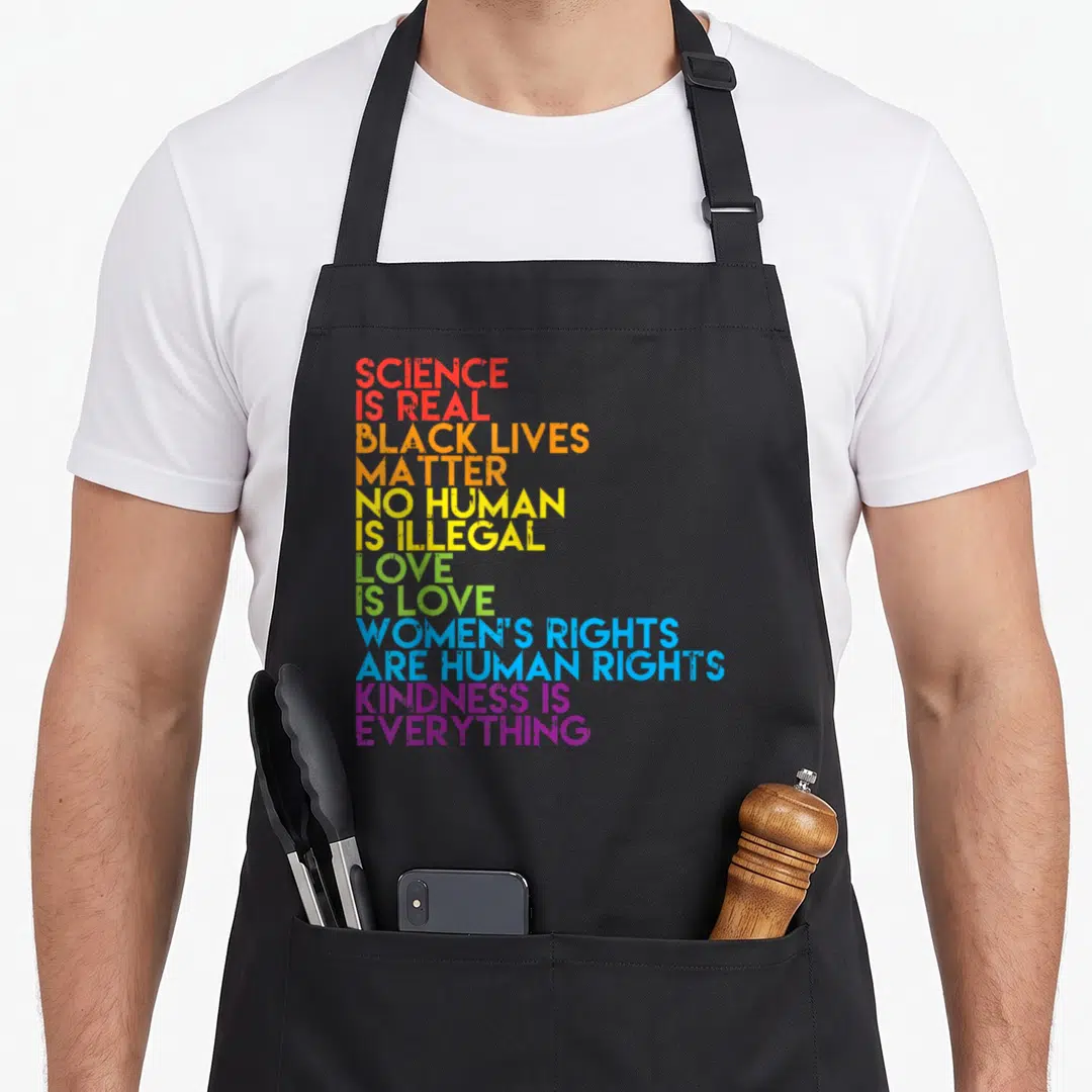 Matter science apron - Rainbow stacked text: Science Is Real, Black Lives Matter, No Human Is Illegal, Love Is Love — shown on a black cotton canvas apron against a white background