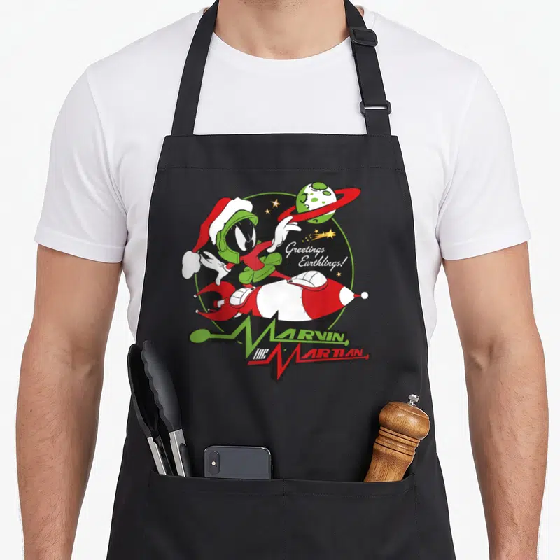 Marvin christmas apron - Marvin the Martian in Santa hat riding red rocket with Greetings Earthlings text — shown on a black cotton canvas apron against a white background