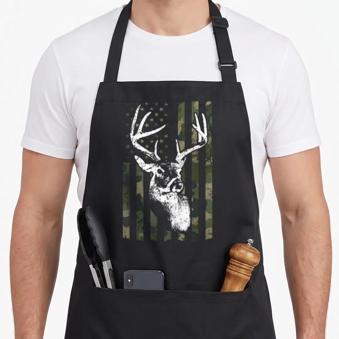 Funny camouflage american flag apron - White deer head silhouette over vertical olive camo stripes and stars — shown on a black cotton canvas apron against a white background