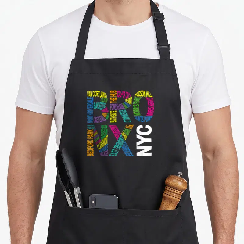 Boogie bronx new york apron - BRONX NYC text composed of neighborhood names in yellow blue pink green white — shown on a black cotton canvas apron against a white background