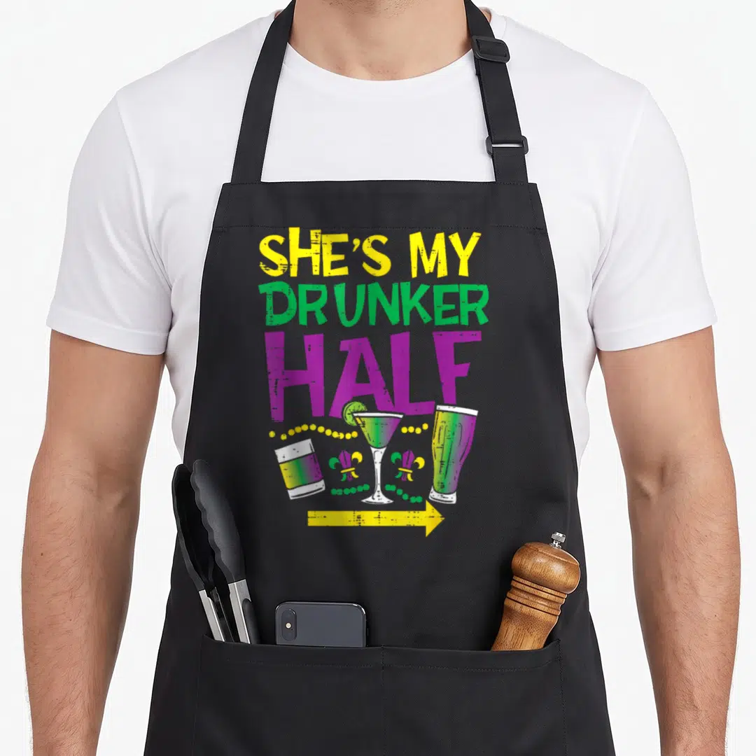 Drunker mardi gras aprons - Stacked text She's My Drunker Half above three drinks, two fleur-de-lis, beads, and yellow — shown on a black cotton canvas apron against a white background