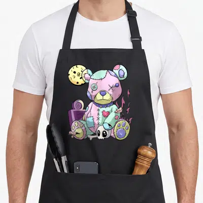Kawaii teddy bear apron - Patched cartoon teddy bear with moon, skull, bone, and purple flames in pink, purple, blue — shown on a black cotton canvas apron against a white background