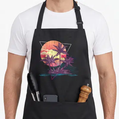 Tropical tree apron - Three purple palm trees against retro sun with geometric triangles and blue water line — shown on a black cotton canvas apron against a white background