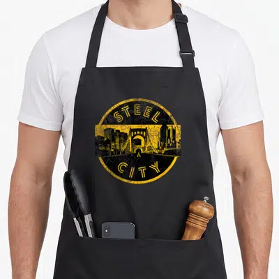 Funny pittsburgh apron - Yellow and black distressed steel city skyline emblem with bridge — shown on a black cotton canvas apron against a white background