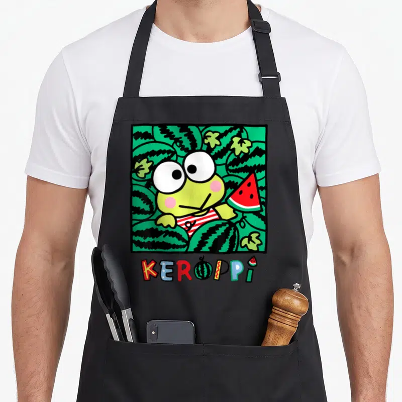 Keroppi watermelon apron - Cartoon frog holding red watermelon slice inside green patterned square with KEROPPI text — shown on a black cotton canvas apron against a white background