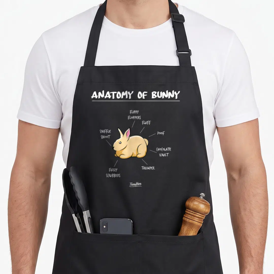Anatomy bunny apron - Tan cartoon rabbit diagram with labels Flippy Floppers Poof and Chocolate Vault — shown on a black cotton canvas apron against a white background
