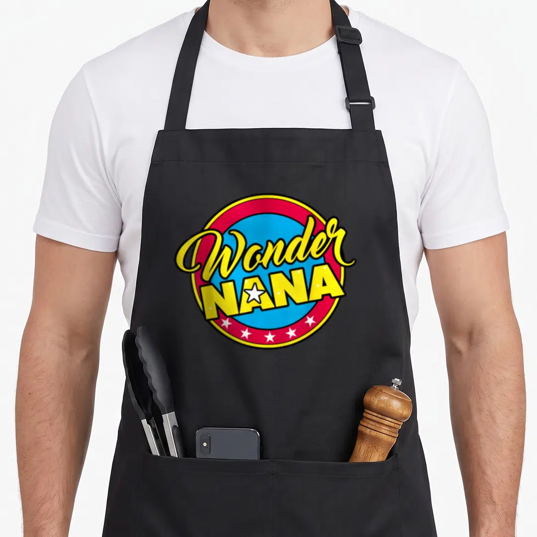 Superhero nana aprons - Wonder NANA text in yellow over red and blue circle with white stars replacing letters — shown on a black cotton canvas apron against a white background