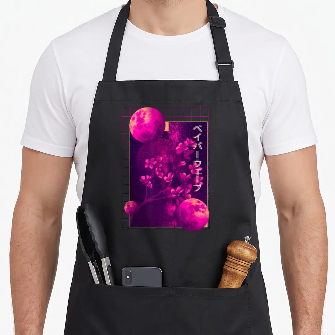 90s cherry print apron - Three pink moons and cherry blossoms over pink grid with vertical Japanese text — shown on a black cotton canvas apron against a white background