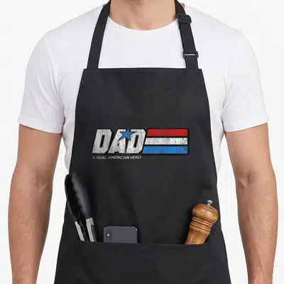 Hero bomber apron - Dad A Real American Hero distressed text with blue star and red white blue stripes — shown on a black cotton canvas apron against a white background