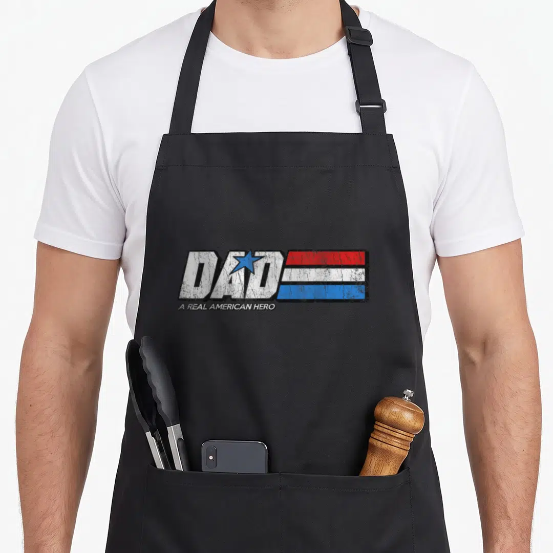 Hero bomber apron - Dad A Real American Hero distressed text with blue star and red white blue stripes — shown on a black cotton canvas apron against a white background
