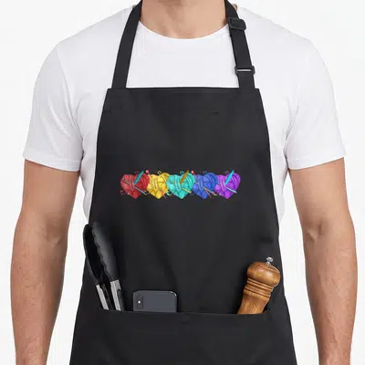 Yarn crochet knitting apron - Five heart-shaped yarn balls in red, yellow, cyan, blue, purple with crochet hooks — shown on a black cotton canvas apron against a white background