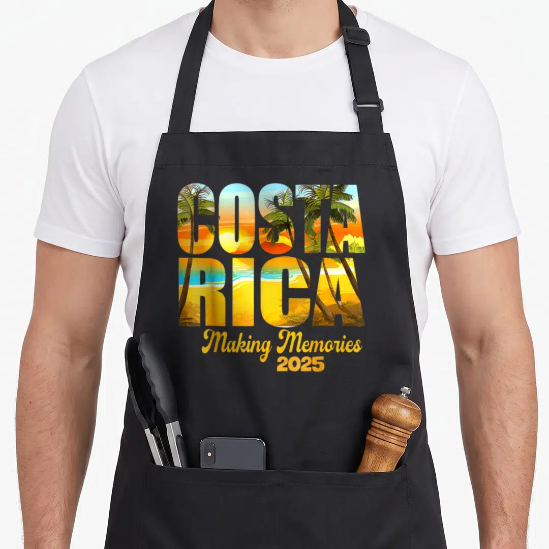 Costa memory apron - Stacked Costa Rica text filled with palm trees and sunset colors above Making Memories 2025 script — shown on a black cotton canvas apron against a white background