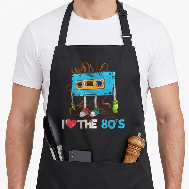 80s 1980s apron - Blue cassette tape character with limbs and I love the 80s text in cartoon style — shown on a black cotton canvas apron against a white background