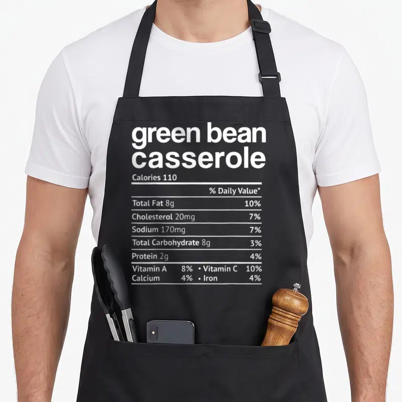 Bean thanksgiving apron - White typography nutrition label listing green bean casserole calories and vitamins — shown on a black cotton canvas apron against a white background
