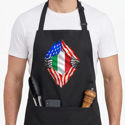 Flag root italy apron - Two grey hands rip USA flag to reveal Italian flag stripes — shown on a black cotton canvas apron against a white background