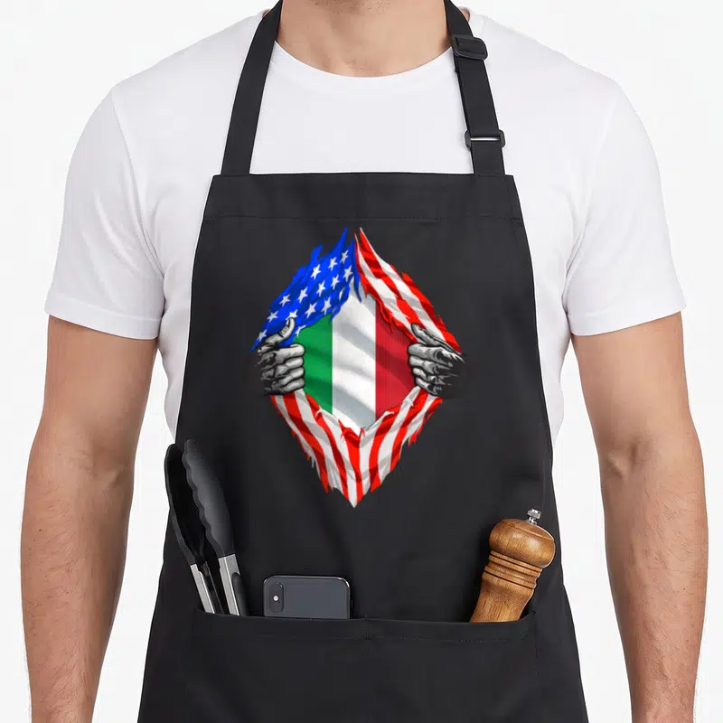 Flag root italy apron - Two grey hands rip USA flag to reveal Italian flag stripes — shown on a black cotton canvas apron against a white background