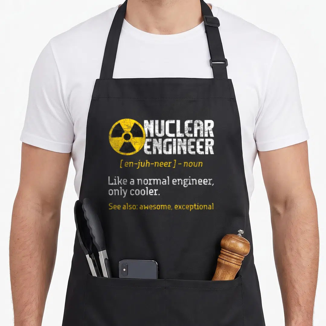 Radioactive engineer apron - Yellow radiation symbol next to white text defining nuclear engineer as cooler than normal — shown on a black cotton canvas apron against a white background
