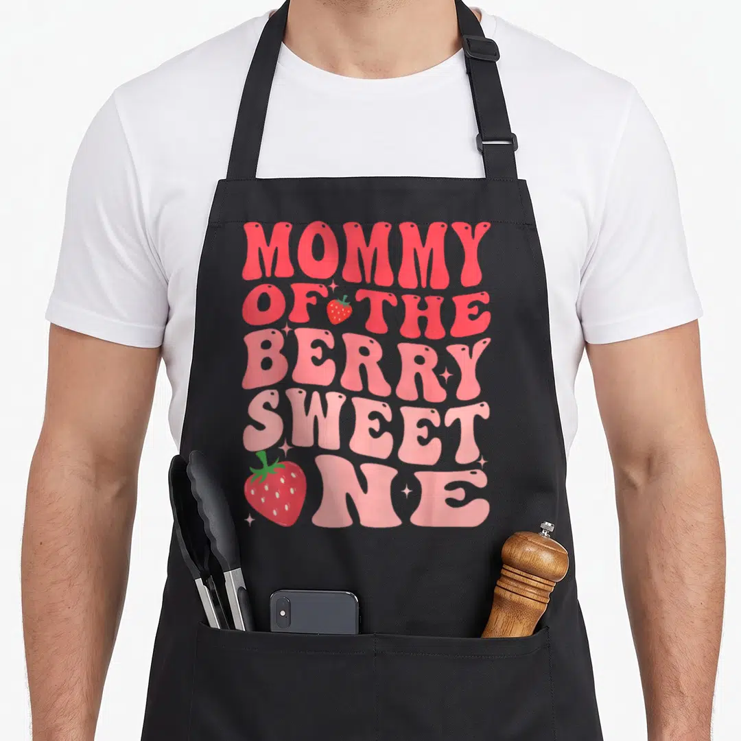 Berry sweet strawberry apron - Retro pink text Mommy of the Berry Sweet One with strawberries and stars — shown on a black cotton canvas apron against a white background