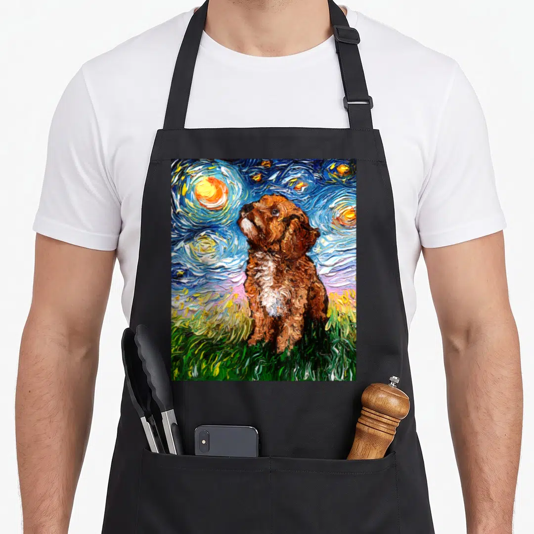 Cavapoo starry dog apron - Brown dog on green grass under swirling blue night sky with yellow stars and moon — shown on a black cotton canvas apron against a white background