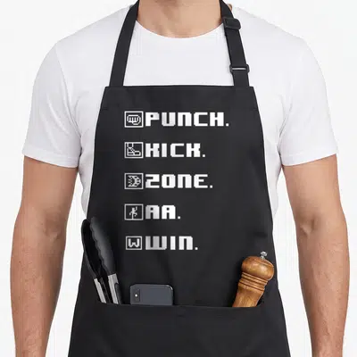 Punch game aprons - White pixel text PUNCH KICK ZONE AA WIN stacked vertically with small square icons — shown on a black cotton canvas apron against a white background