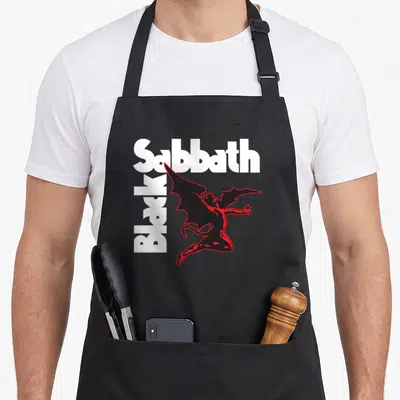 Funny creature black sabbath apron - White and red text with a black devil figure holding a star — shown on a black cotton canvas apron against a white background