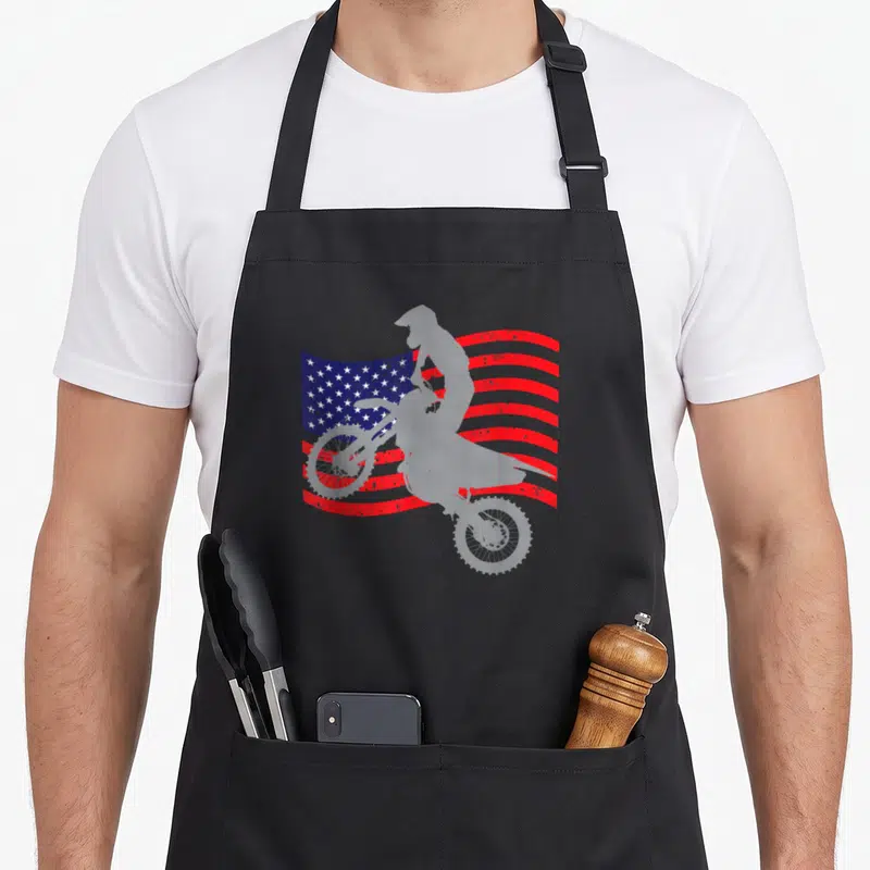 Dirt youth bike apron - White motocross rider silhouette on distressed red white and blue flag — shown on a black cotton canvas apron against a white background